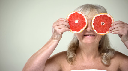 Optimistic aging lady closing eyes with grapefruit slices, cosmetic procedures