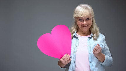 Playful old lady holding pink heart, concept of love at any age, Valentines day