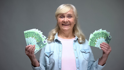 Joyful senior female showing euro banknotes, quick loan service, wealth concept