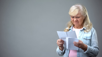 Upset aged female receiving letter from bank, surprised with debt information