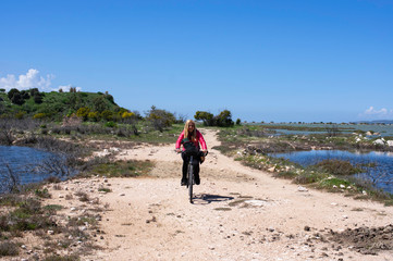 A blonde girl riding bicycle on a path through a lake
