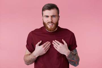 Photo of bearded young man with tattooed hand, standing insulted and intense pointing at himself...