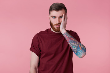 Portrait of sad bored young man with tattooed hand, propping up his head, isolated over pink background. © timtimphoto