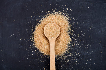 Brown cane sugar in wooden spoon on black board background.