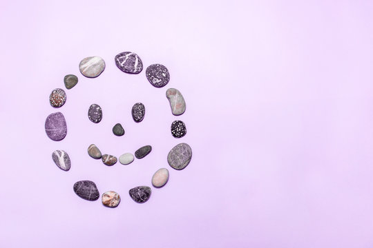 Beach pebbles made into a smiling face on a purple background. Concepts for health, happiness, healing, wellness. copy space. top view.