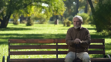 Obraz premium Old man with walking cane sitting on bench, resting after walking in park