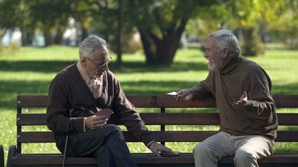 Mature friends playing cards having fun in park, active lifestyle, retirement