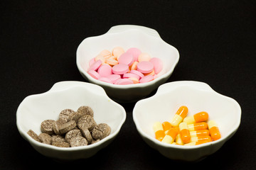 Capsules, tablets and gelatin-shaped medicines in oyster-shaped bowls on black background