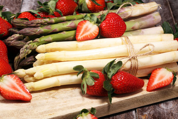 White and green asparagus with strawberries on wood