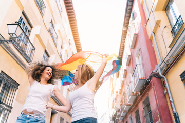 Couple lesbian woman with gay pride flag on the street of Madrid city