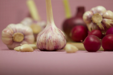 Healthy vegetables on a pink background. Fresh garlic (allium, Bulbus Allii Sativ) is a real storehouse of nutrients and trace elements. Red sweet onions (solaninum) - natural antioxidant. Red radish 