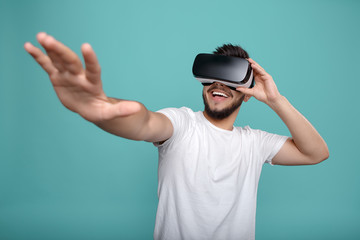 Young handsome bearded man wearing virtual reality goggles in studio on colorful background. Smartphone using with VR headset.