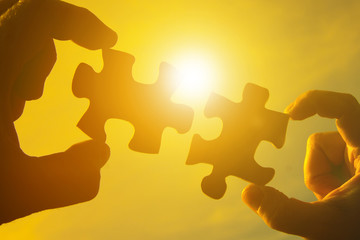 Two hands connect two pieces of the puzzle against the sky and glare of the sun at sunset. Business...