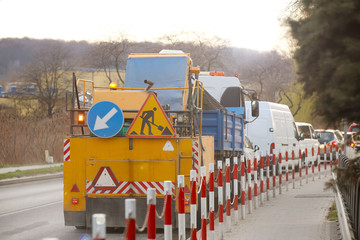 An orange street-cleaning machine stands in a traffic jam near the sidewalk designated by signal...