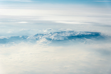 Top view of white clouds between which you can see high mountains