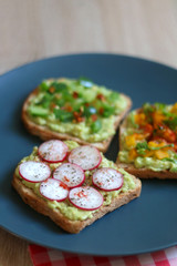 Three slices of toast with mashed avocado and various vegetable and herb toppings. Selective focus.
