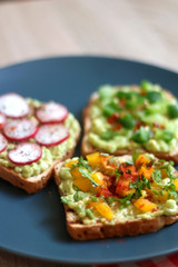 Three slices of toast with mashed avocado and various vegetable and herb toppings. Selective focus.