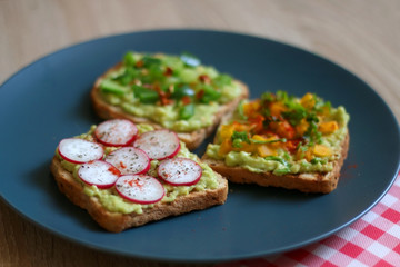 Three slices of toast with mashed avocado and various vegetable and herb toppings. Selective focus.