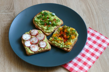 Three slices of toast with mashed avocado and various vegetable and herb toppings. Selective focus.