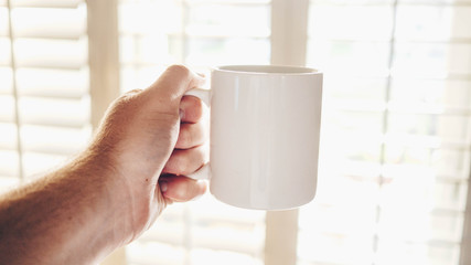 Fototapeta na wymiar Hand Holding Coffee Mug in Morning Sun