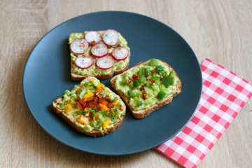 Three slices of toast with mashed avocado and various vegetable and herb toppings. Selective focus.