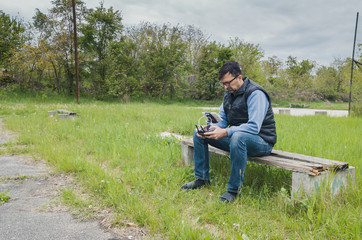 Naklejka na ściany i meble A man sits on the bench and remotely controls the dron