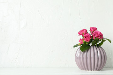 Vase with pink roses and space for text on white table against light background