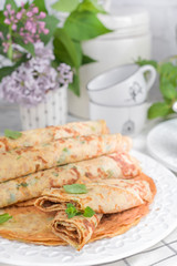 Pancakes with dill and white sauce on a light background. Spring flowers and tableware for breakfast.