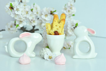 Easter composition on white background.Ceramic rabbit , two eggs and homemade cookies in the form of bunnies.apricot flowers