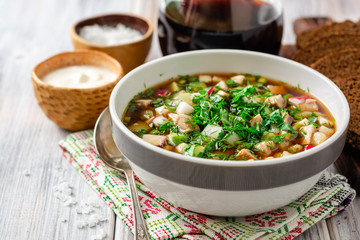 Traditional Russian summer cold soup okroshka with kvass in bowl on wooden background. Selective focus.