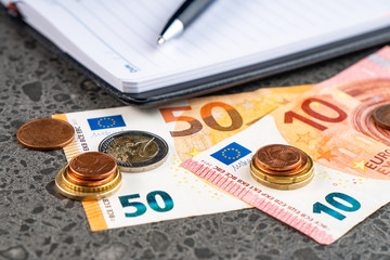 Money euro, notebook and pen on stone background