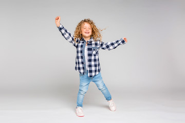 baby girl blonde in plaid shirt and jeans on light background, happy baby on light background