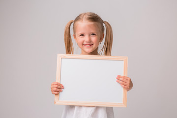 Fototapeta premium girl holding a white Board .Cute little girl with a white sheet of paper.white background.copy spase.Little girl holding an empty white sheet,place for text