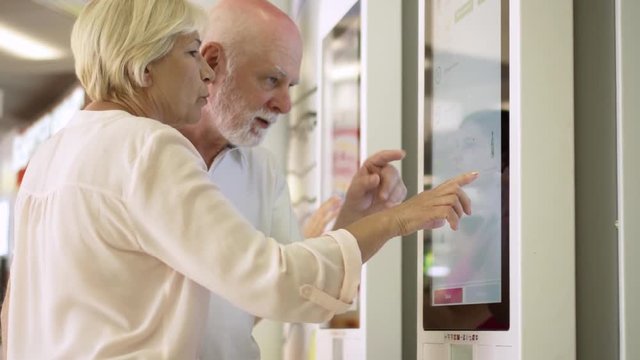 MOSCOW, RUSSIA- CIRCA August 2018: Senior couple ordering food via self-service machine at fast-food chain restaurant Mcdonald's. Active modern life after retirement. Editorial use only.