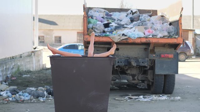 Legs sticking out of the garbage can. The truck body is filled with garbage.