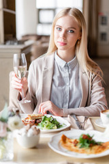 Portrait of a beautiful young elegant blonde woman in the cafe with a glass of champagne.