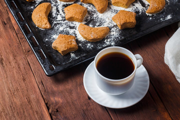 Handmade cookies on a baking sheet and a cup with hot tea or coffee on a wooden background. The concept of homemade culinary skills.