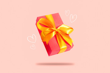 Flying gift box on a light pink background with hearts. Holiday concept, gift, sale, wedding and birthday.