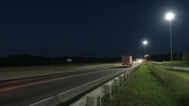 Cars and trucks on the highway. Suburban car traffic on the road at night. Dark forest in the background. Night lighting. Lanterns at night along the road. Dark background. Blue sky.