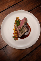 Platillo servido en plato blanco sobre mesa de madera, filete crudo con semillas y guarnición de verduras