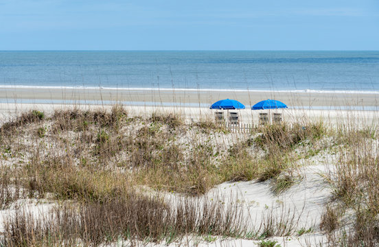 A beachfront view of two blue beach umbrellas and chairs