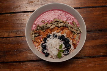 Bowl de Yogurt y açai con pepitas, almendras, mora azul y coco sobre mesa de madera