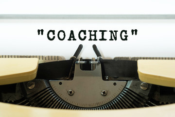 Coaching word typed on a yellow vintage typewriter. Business concept.