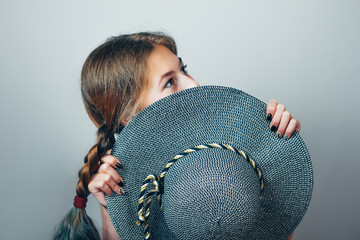 Shy girl on dark grey background. Girl hiding her face behind a round hat.