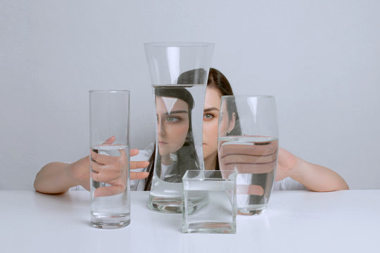 Art Portrait Of Young Attractive Woman. Distorted Reflection In Glass Vases With Water.