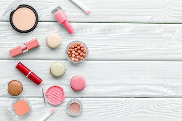 Make-up artist desk with powder, polish, decorative cosmetics and macaroon cookies white background top view mokeup