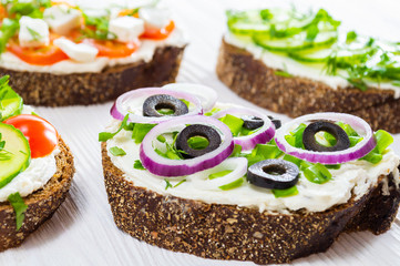 Healthy breakfast: sandwiches with cream cheese and vegetables on white wooden table. Selective focus.