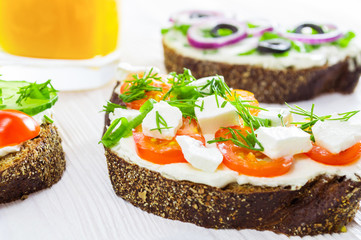 Healthy breakfast: sandwiches with cream cheese and vegetables, and a glass of orange juice. on white wooden table. Selective focus.