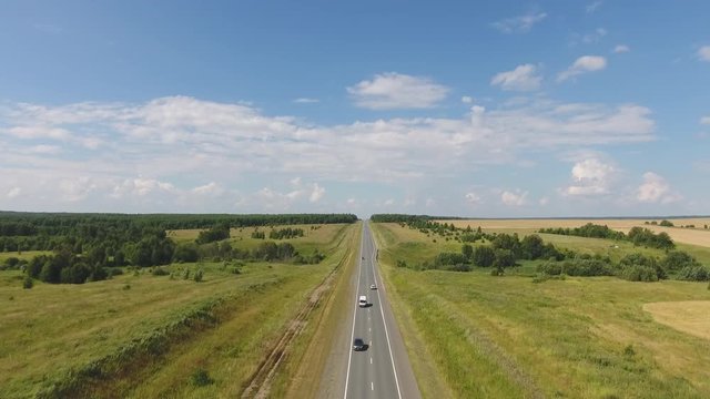 Flying over the straight road. The movement of cars on the road. Top view on the car, forest, field. Summer video from the drone. Rural landscape.