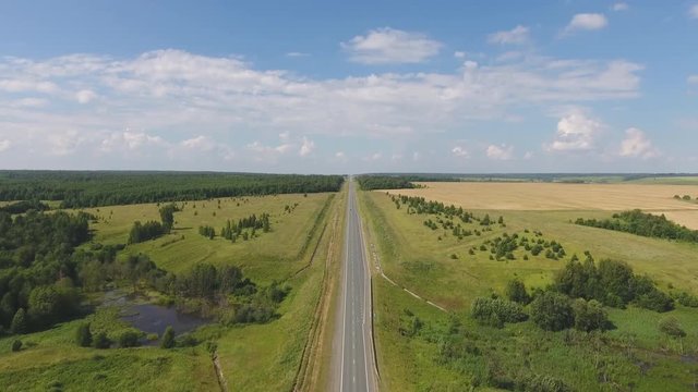 Flying over the straight road. The movement of cars on the road. Top view on the car, forest, field. Summer video from the drone. Rural landscape.
